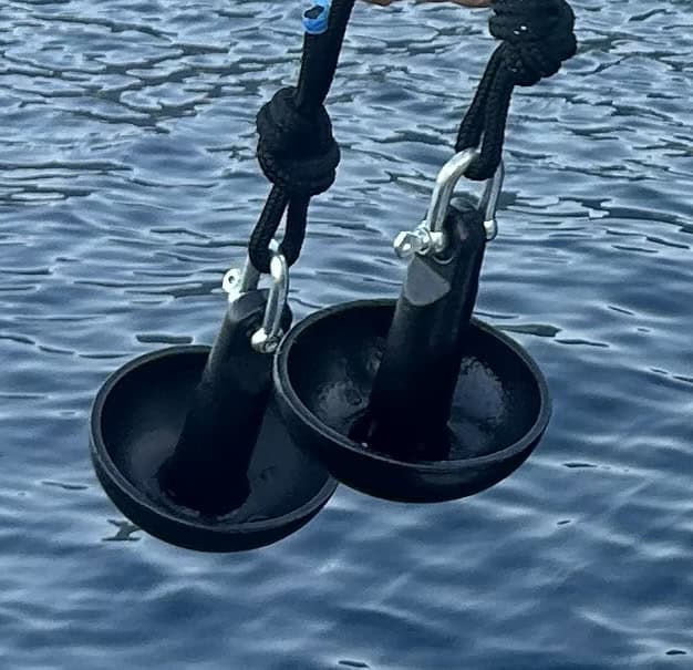 Black steel mushroom boat anchor with water in the background. 