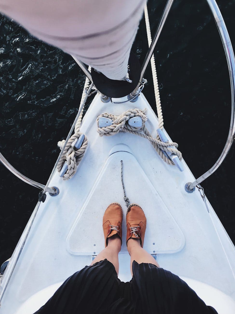 Person standing on the bow of a sailing boat in brown shoes. The surface they are standing on is a non skid paint deck. 