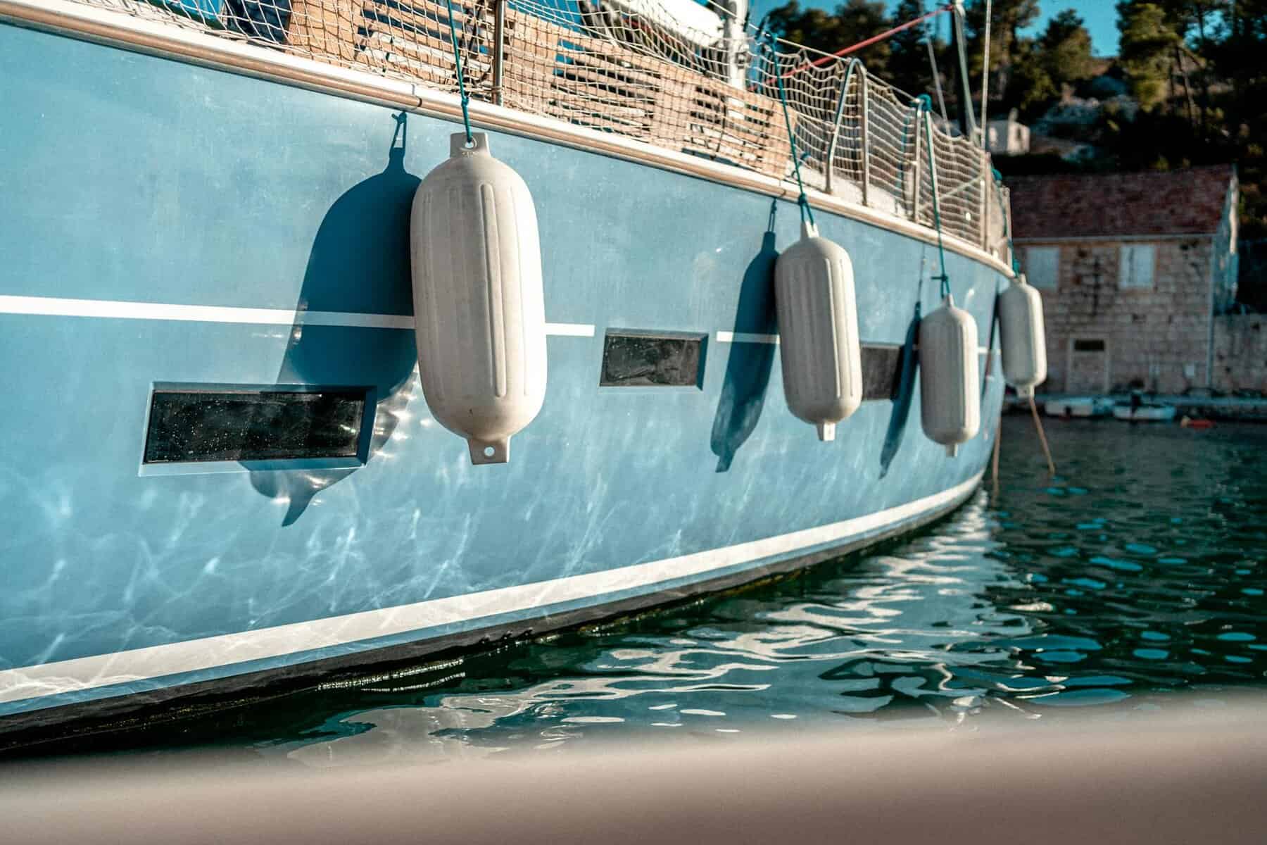 chalky blue boat paint on a sailing yacht hull with white fenders hanging down. 
