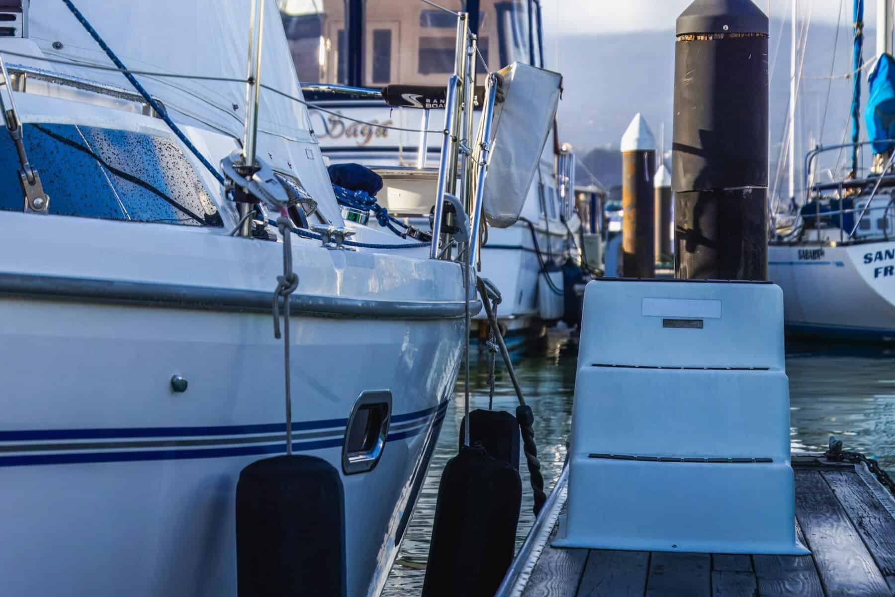 close up of a yacht moored to a pier in the harbor with blue fenders. 