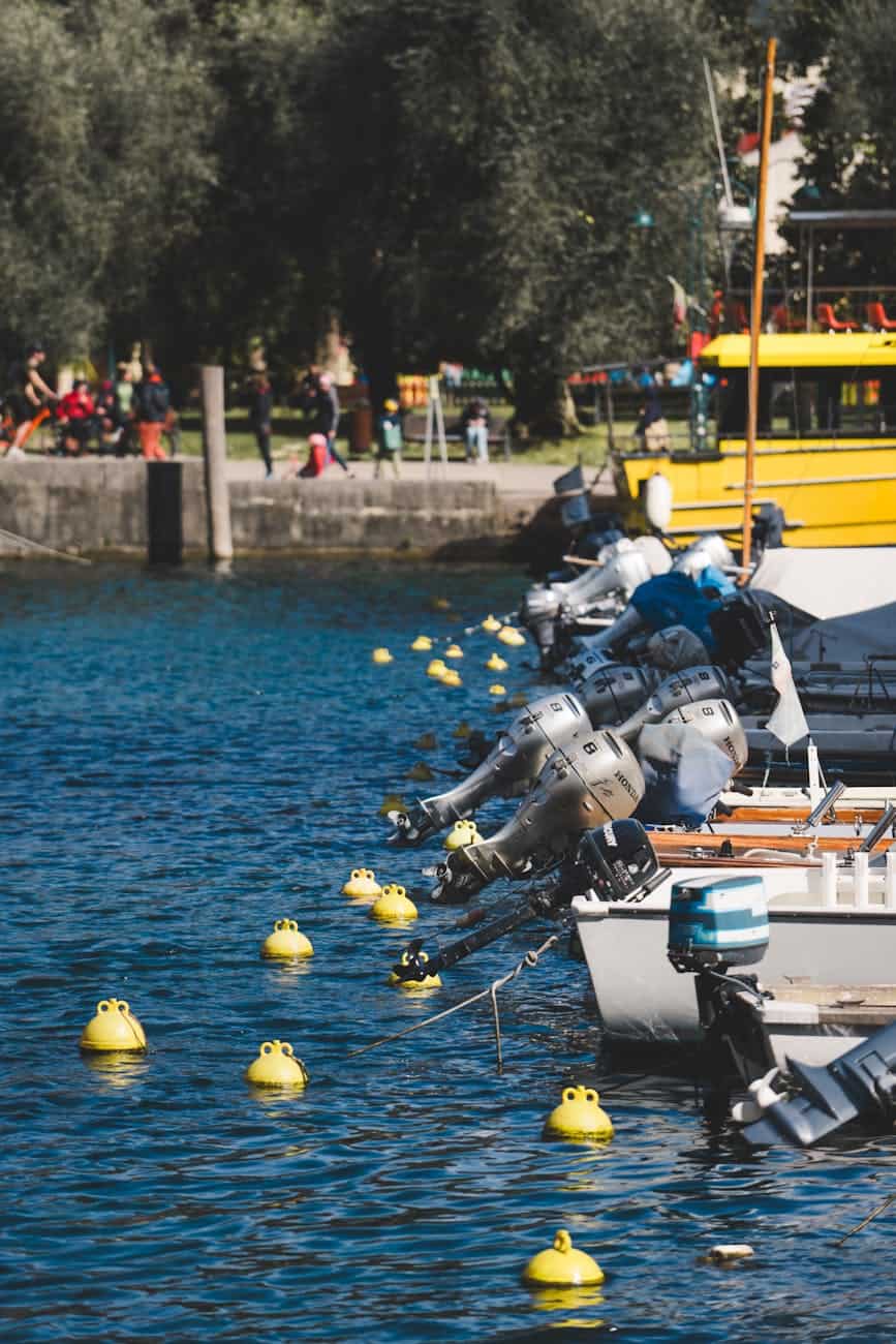 boats aligned along marina with yellow buoys with all outboard engines lifted out of the water. 