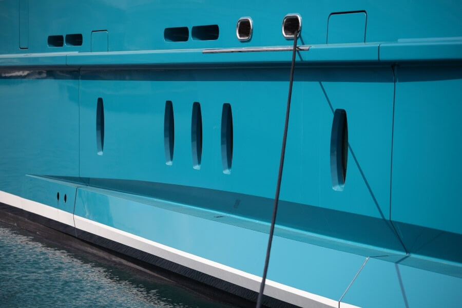 Turquoise blue hull of a super yacht with fender line hanging down the middle. 
