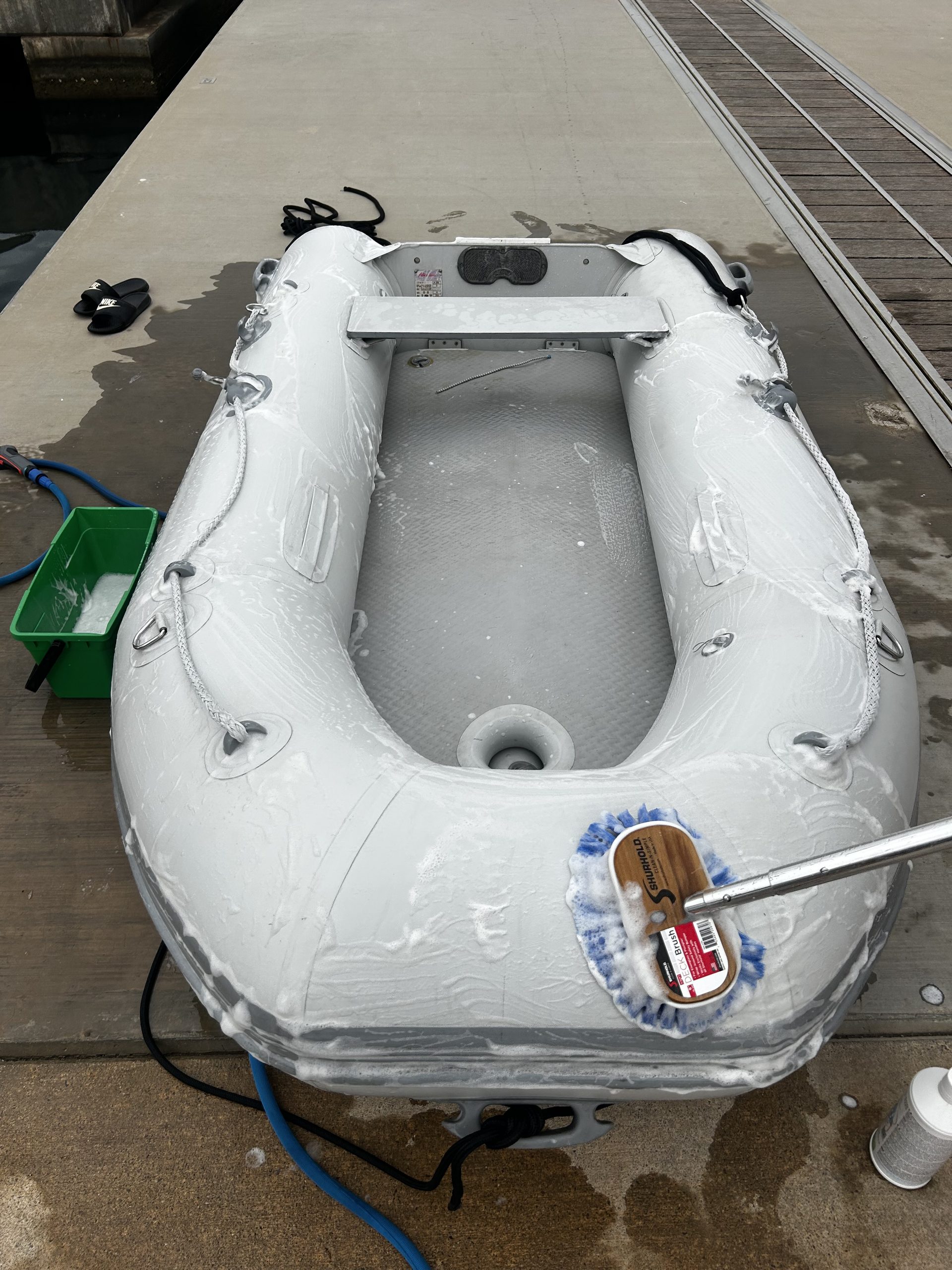 Inflatable boat dinghy being cleaning on the dock with soap and a blue brush. 